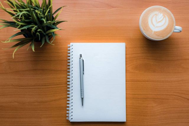 Ce que propose Au Jardin Malin et comment il est fait Carnet à spirale et stylo sur un bureau en bois, à côté d'une plante verte et d'un café