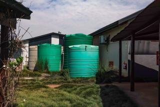 Trois cuves vertes de récupération d'eau de pluie à côté d'une maison
