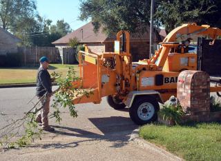 Broyeur de branches en action devant une maison, branches engagées dans la trémie
