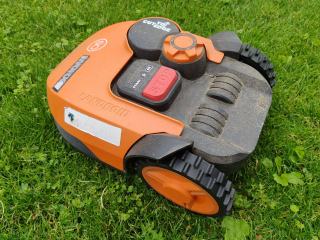 Robot tondeuse orange posé sur un gazon fraîchement coupé