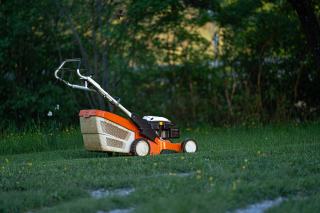 Tondeuse à gazon orange et grise arrêtée au milieu d'une pelouse